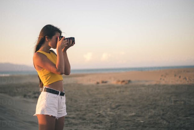 Teenage girl taking photos with camera on the beach at sunset – Stockphoto