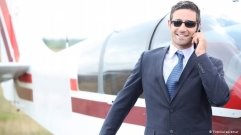 Ein junger Mann mit Sonnenbrille steht telefonierend vor einem Kleinflugzeug