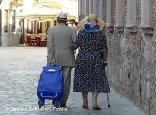 Senioren-Ehepaar mit beim Einkaufen in einer Altstadt. Er zieht einen Einkaufstrolley hinter sich her
