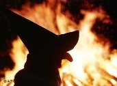 Eine Hexe mit Hut steht vor einem Feuer