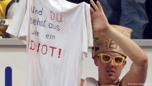 Ein Mann hält ein T-Shirt hoch mit der Aufschrift: Und du siehst aus wie ein Idiot