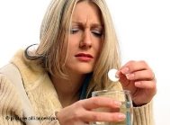 Eine Frau löst mit schmerzverzerrtem Gesicht eine Aspirin-Tablette in einem Glas mit Wasser auf
