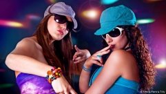 Zwei Frauen mit Sonnenbrille und Kappe tanzen in einer 
Disco